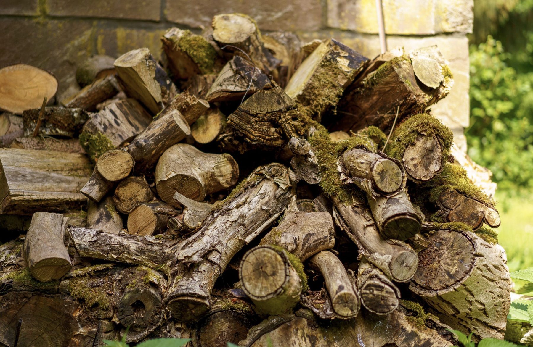 Aufgeschichteter Stapel Brennholz vor einer Bruchsteinmauer