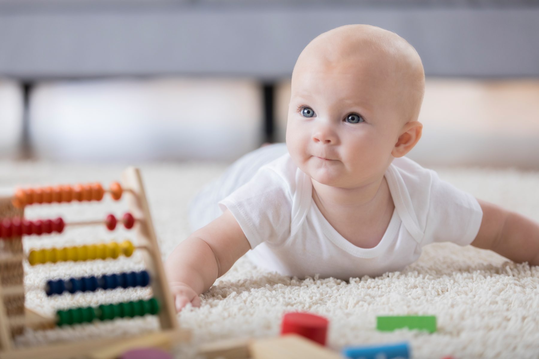 Baby auf einem hellen Teppich neben einem bunten Holz-Abakus